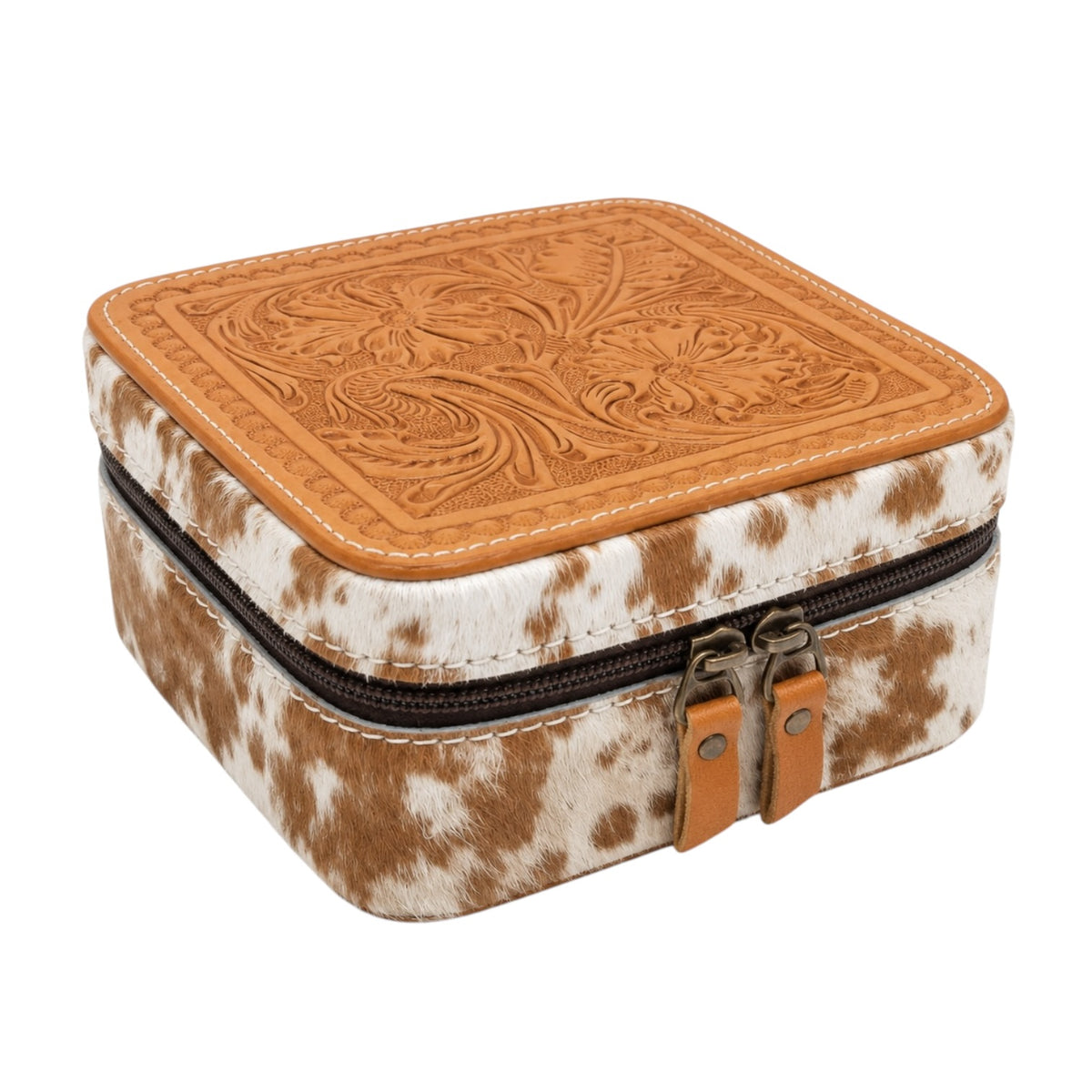 A square jewelry box with a brown and white cowhide patterned body, a tan tooled leather lid, and dual zipper pulls, shown on a plain white background.