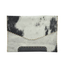 A rectangular envelope-style clutch bag made from black and white cowhide, featuring a stitched v-shaped fold-over flap and a dark gray faux-leather patch at the bottom, shown on a plain white background.