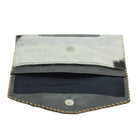 A small leather pouch or wallet shown open on a plain white background. The exterior is made of light gray to off-white hair-on-hide leather with dark black hair showing through, finished with tan whipstitching along the edges.