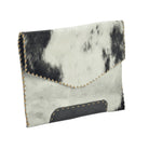 A small envelope-style clutch bag made from black-and-white cowhide, with visible tan stitching along the edges and a dark brown patch on the front, shown on a plain white background.
