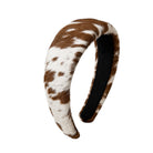A curved headband featuring a brown and white cowhide pattern on the exterior, with a black fabric lining visible on the inner side, set against a plain white background.