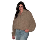 Woman wearing a brown fuzzy sweater and blue jeans against a plain background