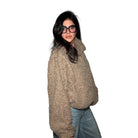 Person wearing a beige sweater and glasses against a plain wall