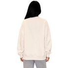 A person viewed from the back wearing an oversized cream sweatshirt and light gray pants against a plain white background.