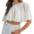 a woman wearing a cream embroidered top with white jeans