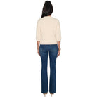 A woman shown from the back wearing a cream three-quarter sleeve top and dark blue flare jeans, standing against a plain white background.