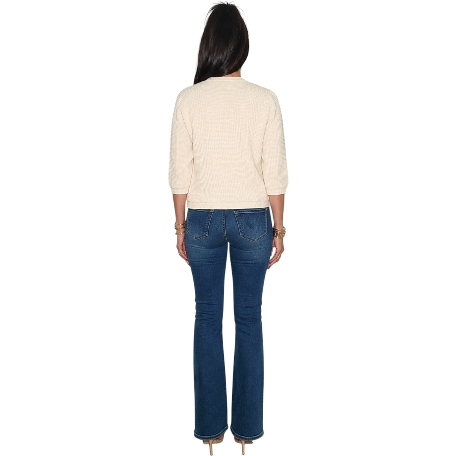 A woman shown from the back wearing a cream three-quarter sleeve top and dark blue flare jeans, standing against a plain white background.