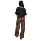 A woman shown from the back wearing a black short-sleeve top and brown wide-leg pants, standing against a plain white background.