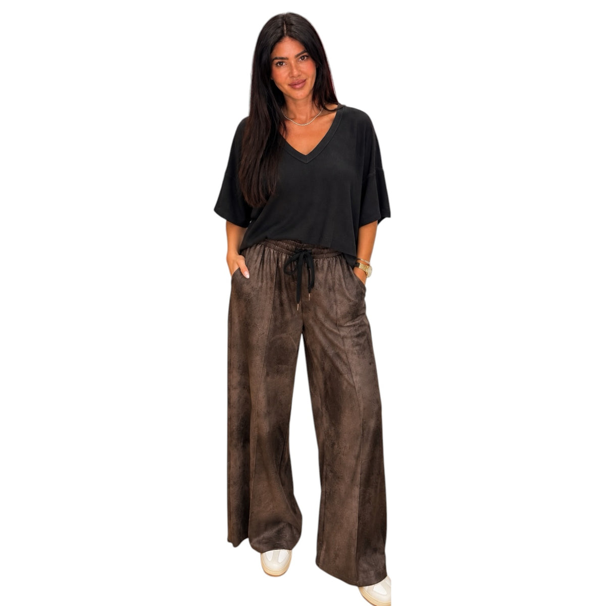 A woman modeling a black short-sleeve V-neck top with brown textured drawstring pants against a plain white background.