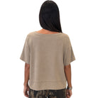 A woman viewed from the back wearing a loose, short-sleeve beige top and camouflage-patterned pants against a plain white background.