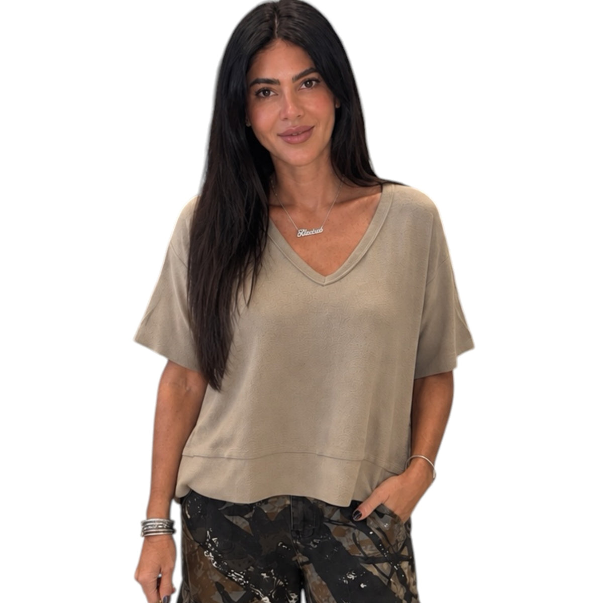 A woman modeling a beige short-sleeve V-neck top with a relaxed fit, paired with camouflage pants, against a plain white background.