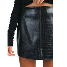 Black crocodile-textured leather skirt worn by a person on a white background