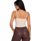 A woman shown from the back wearing a cream-colored textured knit camisole top with thin straps and a scalloped hem, paired with brown faux-leather pants, against a plain white background.