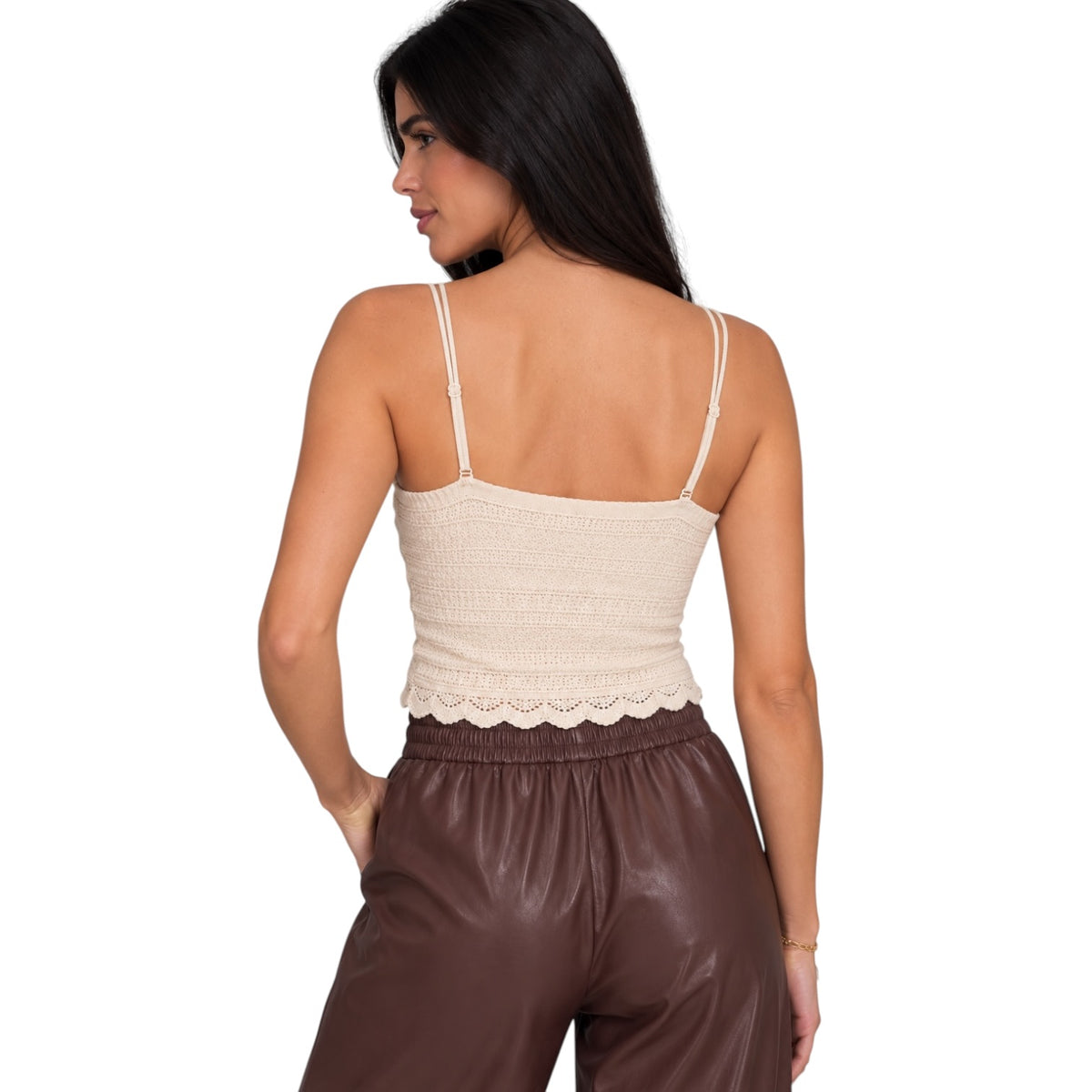 A woman shown from the back wearing a cream-colored textured knit camisole top with thin straps and a scalloped hem, paired with brown faux-leather pants, against a plain white background.