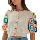 Woman wearing a beige crochet cardigan with colorful flower patterns on sleeves