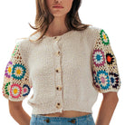 Woman wearing a beige knit cardigan with colorful floral sleeves on a white background
