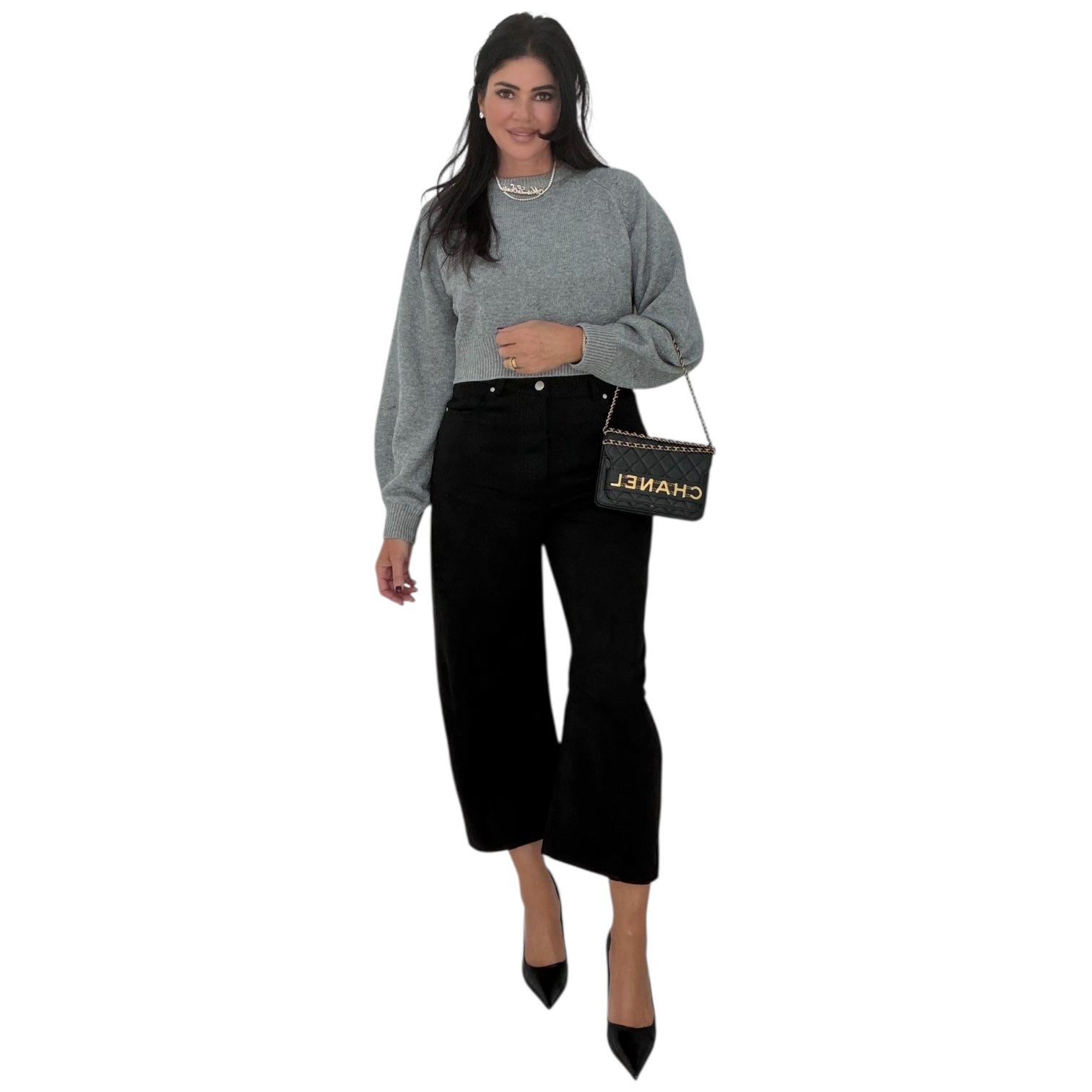 Woman wearing a gray sweater and black pants, holding a Chanel handbag on a white background