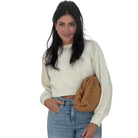 Woman wearing a cream sweater and blue jeans holding a brown bag on a white background