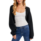 Woman wearing a black cardigan, white tank top, and blue jeans on a white background