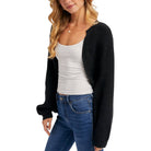 Woman wearing a black cardigan over a white top and blue jeans on a white background