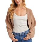 Woman wearing a beige cardigan over a white tank top and blue jeans on a white background