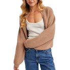 Woman wearing a beige cardigan over a white top and blue jeans on a white background