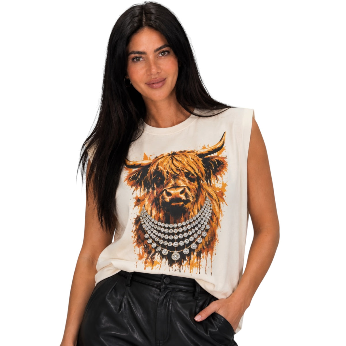 A woman modeling a sleeveless cream-colored t-shirt featuring a large graphic print of a highland cow wearing silver necklaces, paired with black leather pants, against a plain white background.