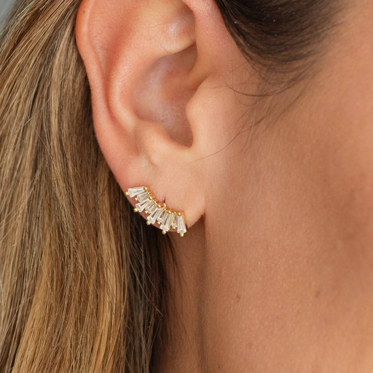 Close-up of an ear wearing a diamond earring with a neutral background