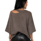 A woman shown from the back wearing a brown knit poncho-style top with a cutout at the upper back and wide short sleeves, paired with black shorts, against a plain white background.