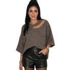 A woman modeling a brown knit top with a diagonal cutout on the chest and wide short sleeves, paired with black leather shorts, against a plain white background.