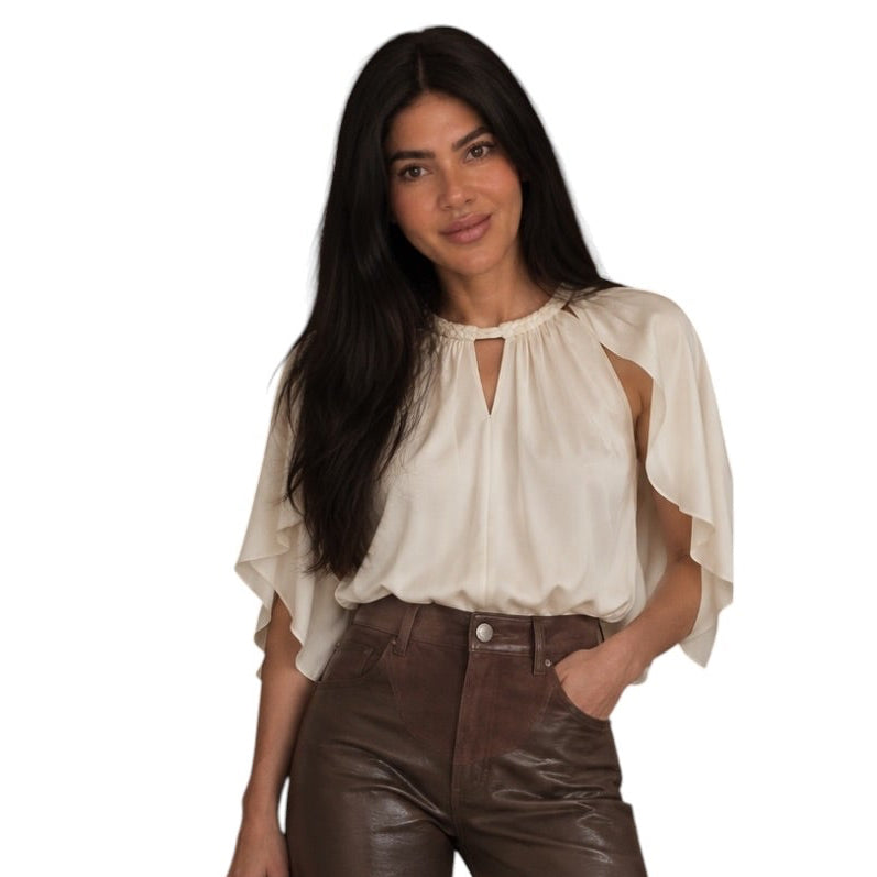A woman modeling a cream-colored blouse with flutter sleeves and high-waisted, wide-leg brown faux-leather pants, holding a black woven handbag against a plain white background.