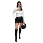 Woman wearing a white long-sleeve sweater, black leather shorts, and black knee-high boots on a white background.