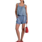Woman wearing a denim romper holding a red handbag on a white background