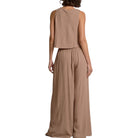 Woman wearing a beige sleeveless top and wide-leg pants on a white background
