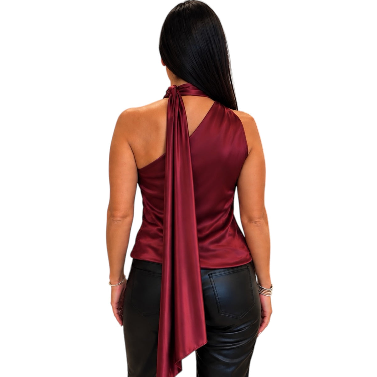 A woman shown from the back wearing a satin halter top in deep burgundy with a long draped tie detail, paired with black faux-leather pants, against a plain white background.