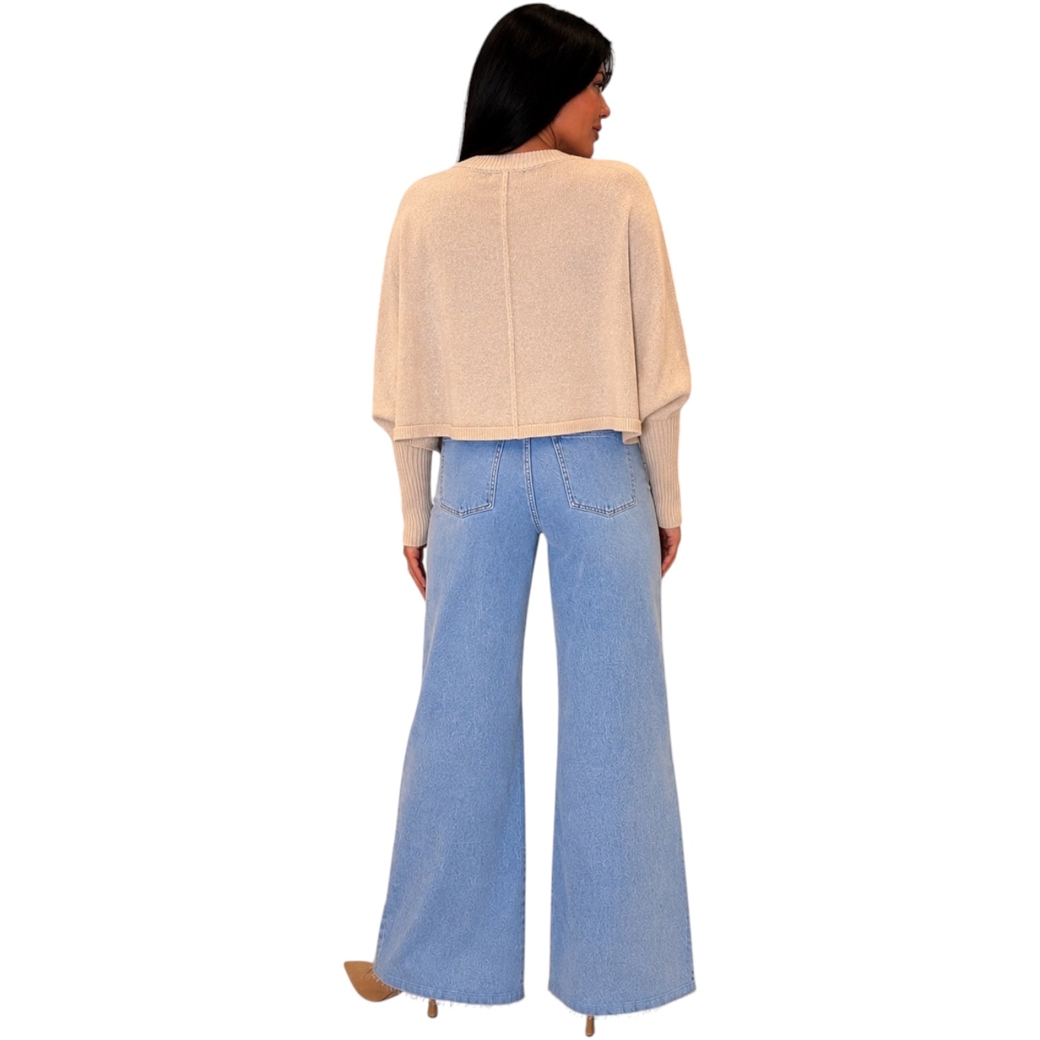 A woman shown from the back wearing a light beige knit cropped sweater and light blue wide-leg jeans, set against a plain white background.