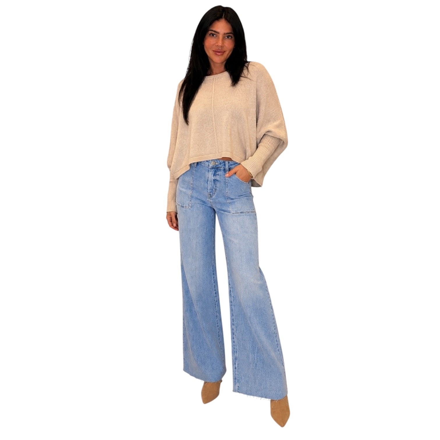 A woman modeling a light beige knit sweater and light blue wide-leg jeans against a plain white background.