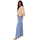 A woman modeling a light beige knit long-sleeve top and light blue wide-leg denim jeans against a plain white background.
