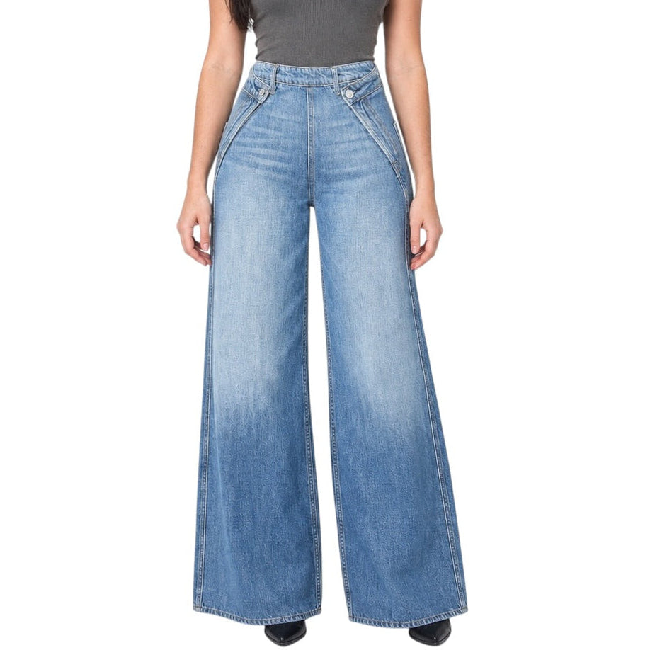 A woman modeling a pair of wide-leg light blue denim jeans with a faded wash, paired with a dark gray sleeveless top, against a plain white background.