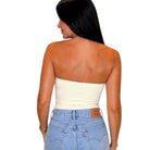 A woman shown from the back wearing a cream-colored strapless bandeau tube top and light blue jeans against a plain white background.
