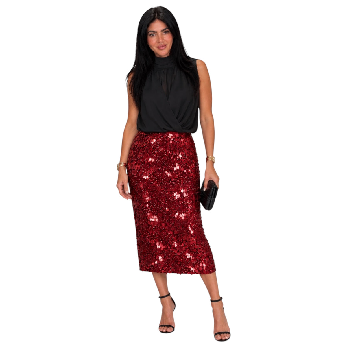 A woman modeling a sleeveless black top and a red sequined midi skirt, holding a small black clutch against a plain white background.