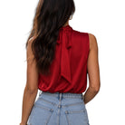 A woman shown from the back wearing a sleeveless deep red satin blouse with a tie-neck detail, paired with light-wash blue jeans, against a plain white background.