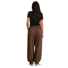 A woman viewed from behind wearing loose brown leopard-print pants, a black short-sleeve top, and brown platform sandals against a plain white background.