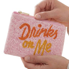 Pink beaded pouch with 'Drinks on Me' text held by a hand against a white background