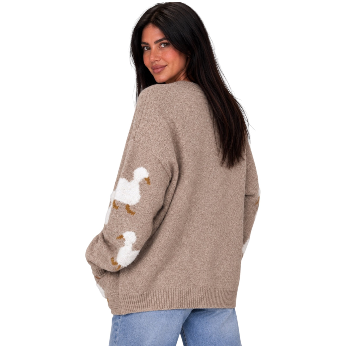 A woman wearing a beige knit sweater with white and brown goose motifs on the sleeves, paired with blue jeans, photographed against a solid white background.