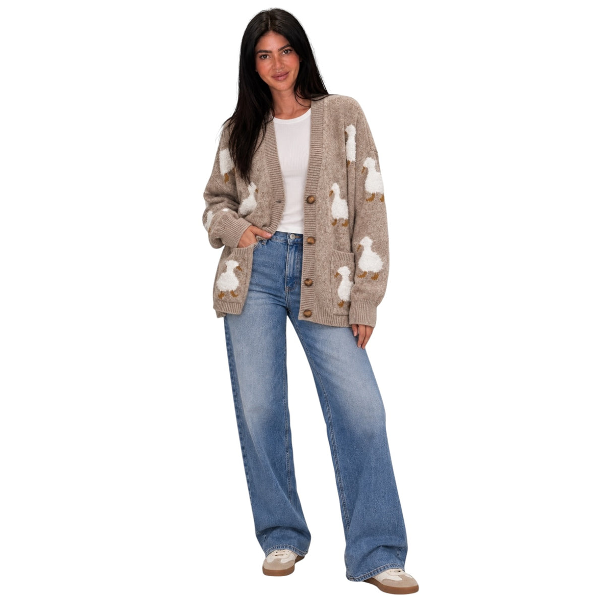 A woman modeling a beige cardigan with white goose motifs, paired with a white t-shirt, wide-leg blue jeans, and white sneakers, set against a plain white background.