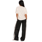 A woman shown from the back wearing a cream short-sleeve t-shirt and black wide-leg athletic pants with white side stripes, set against a plain white background.