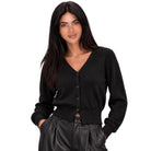 A woman modeling a black long-sleeve V-neck button-up cardigan sweater, paired with black leather-look pants, against a solid white background.