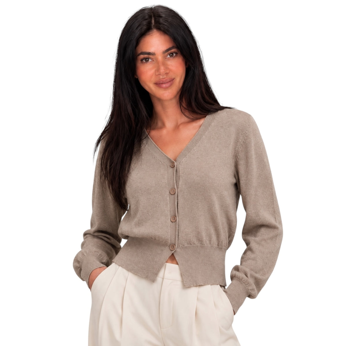 A woman modeling a cropped, long-sleeve knit cardigan in a taupe-beige color with brown buttons, paired with cream-colored trousers, against a solid white background.