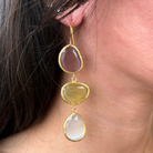 Close-up of a woman wearing gold earrings with three teardrop-shaped stones.